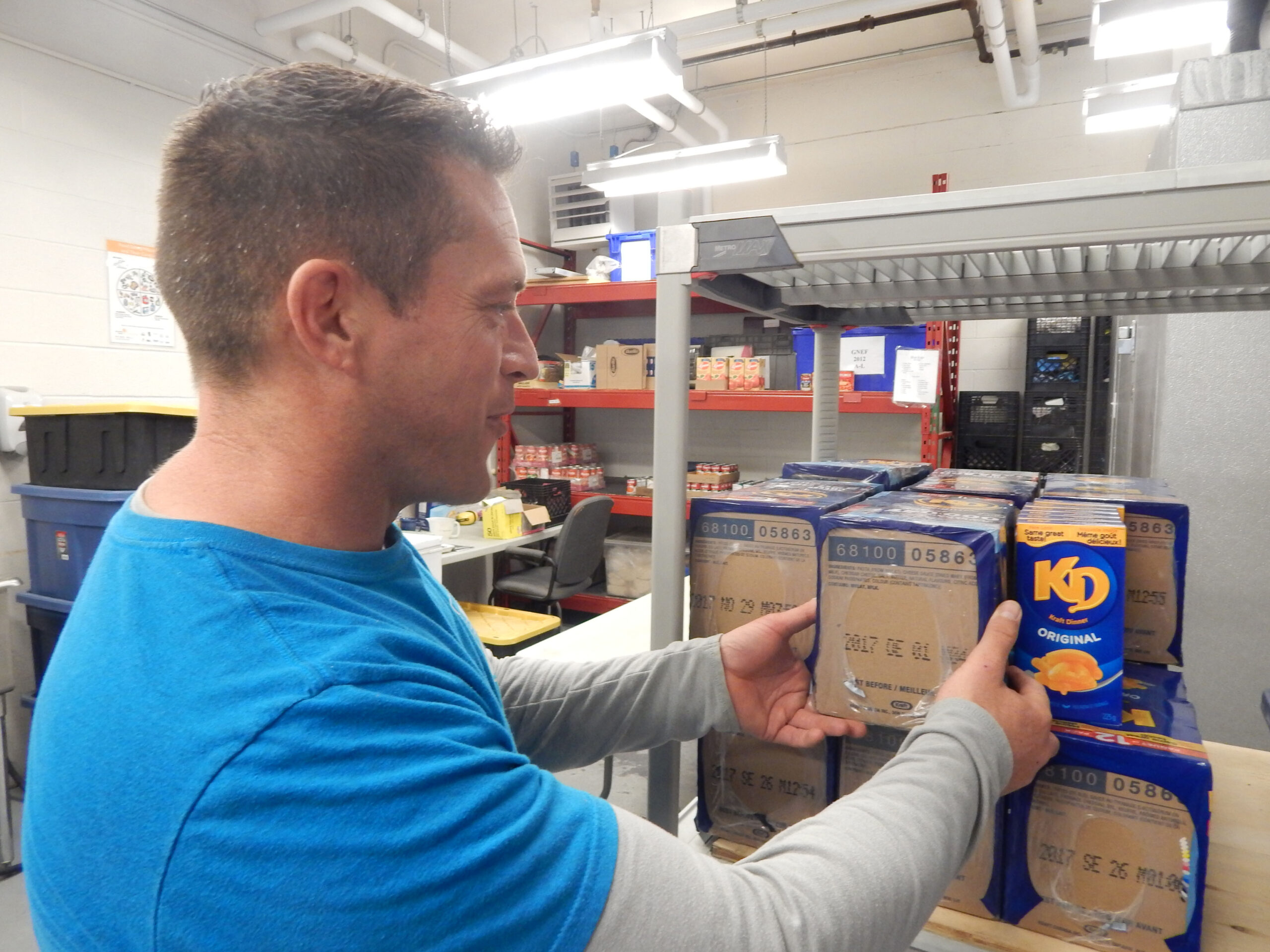 A man working in a food bank places pasta on a shelf