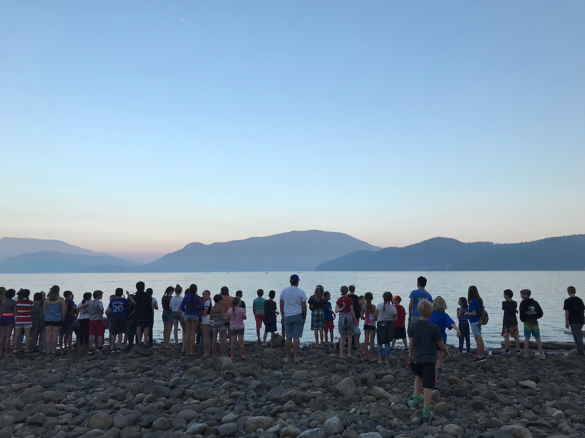 Large group of people on rocky beach looking at ocean and mountains