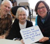 a volunteer smiling with two elderly people