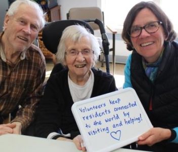 a volunteer smiling with two elderly people