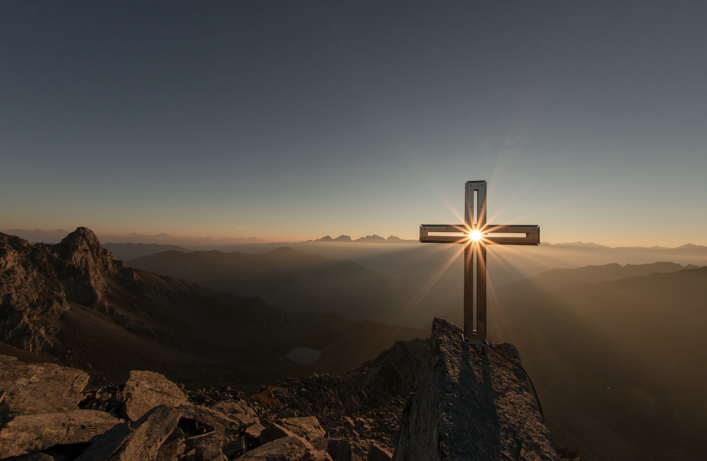 A Cross sitting on a hill as the the sun rises behind