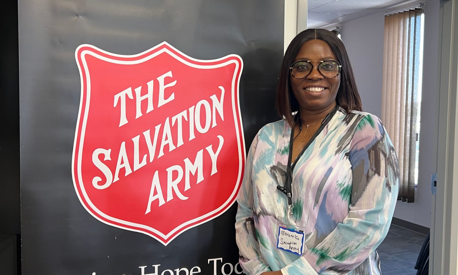 A Practicum Student at Community Justice Services in Winnipeg stands smiling in front of a sign with the Salvation Army logo.