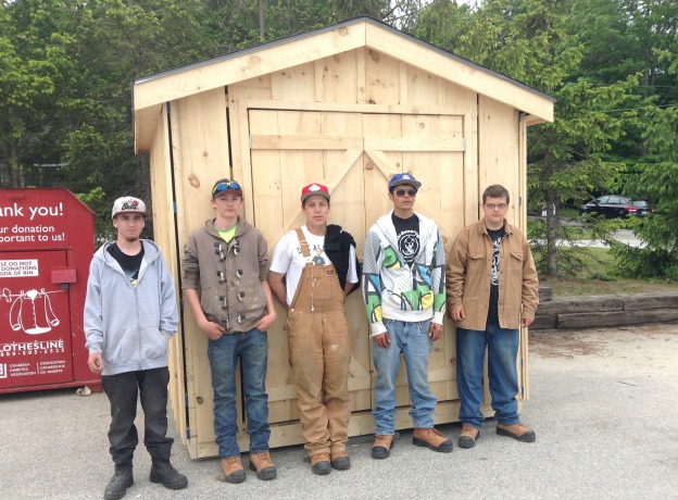 carpentry students stand in front of hand-made shed