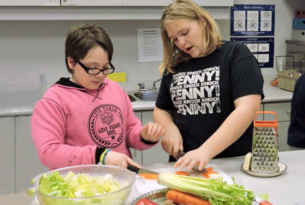 two female participants at cooking camp slice vegetables for a salad