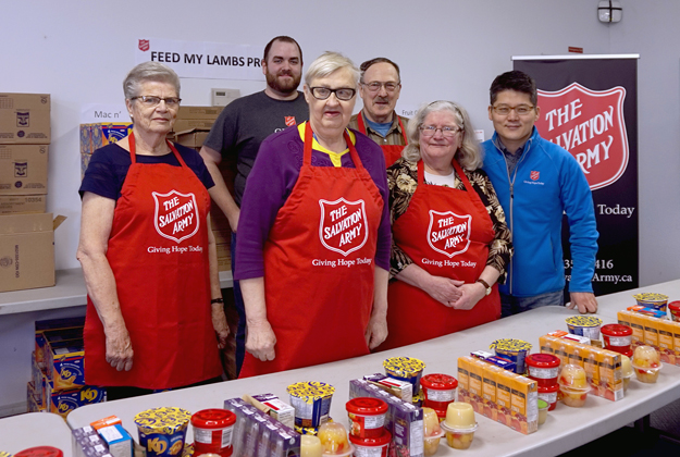 volunteers stand behind a table ready to prepare food for school weekend feeding program