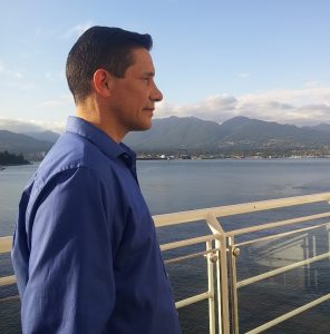 A man wearing a blue shirt looking out out from a pier