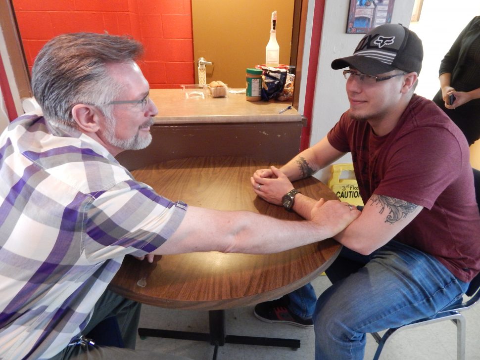 an older man reaching over a table and grabbing a younger man's arm