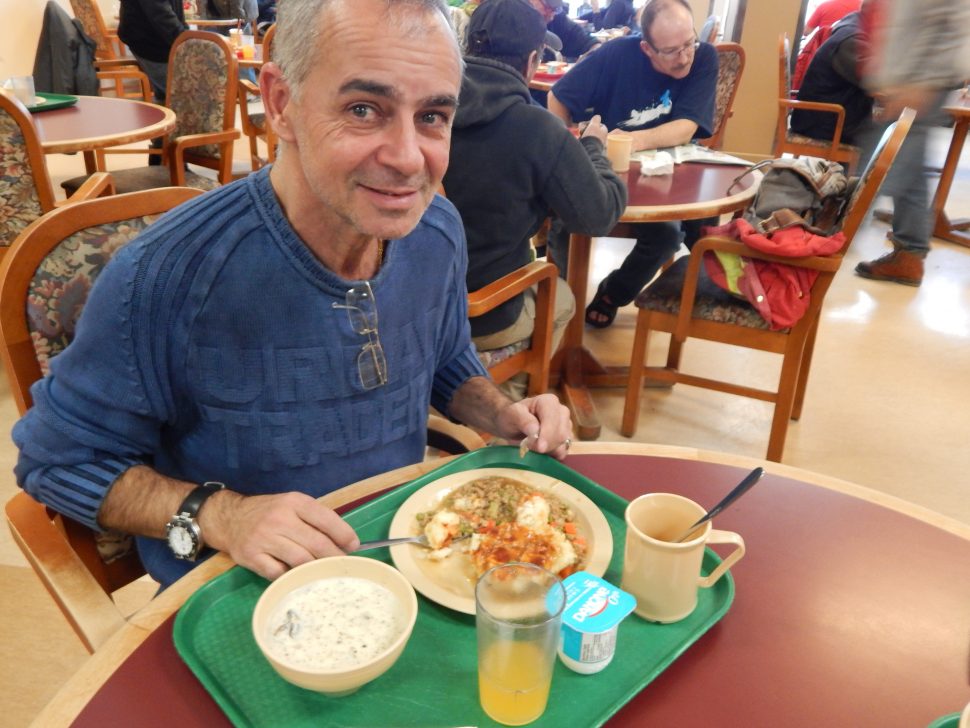 a man sitting at a table eating food off of a green lunch tray