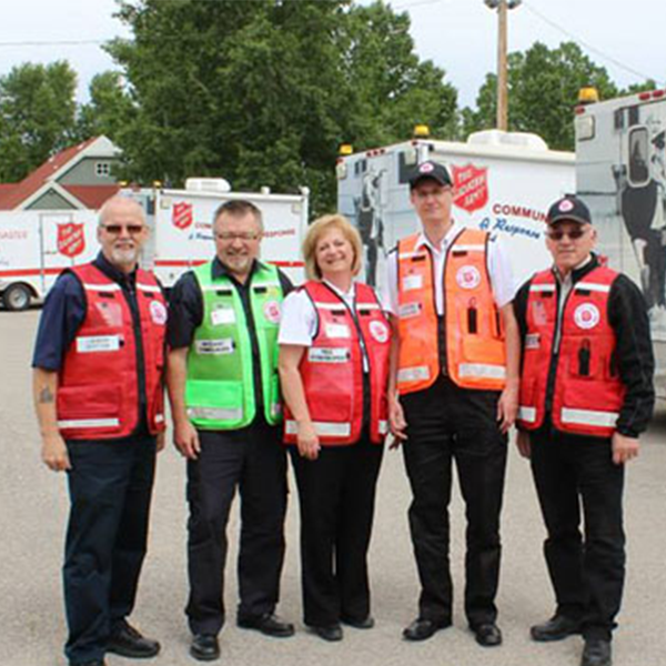 4 men and 1 woman standing in front of salvation army EDS vehicles