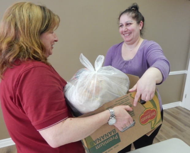 A Salvation Army food bank volunteer handing a box full of food to a smiling food bank guest