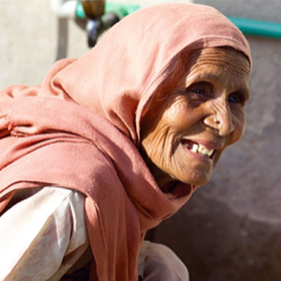 International Development - a women smiling leaning beside a faucet