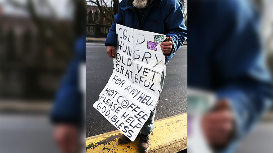 A homeless vet holding a sign that asks for help and hot coffe