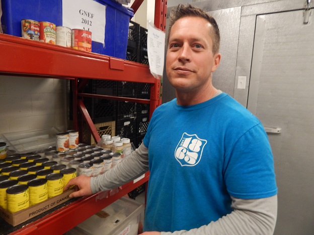 A man named Phil, smiling at the camera, assisting with sorting canned goods at a Salvation Army food bank