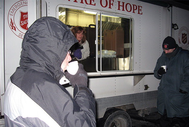 A Salvation Army EDS truck and a profile of a man drinking a hot beverage with his winter jacket and hood on.