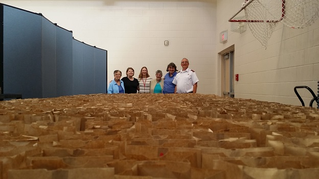 Volunteers stand with hundreds of packed paper lunch bags