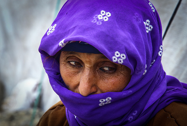 A woman with a cultural head scarf covering her mouth and looking down in cold weather