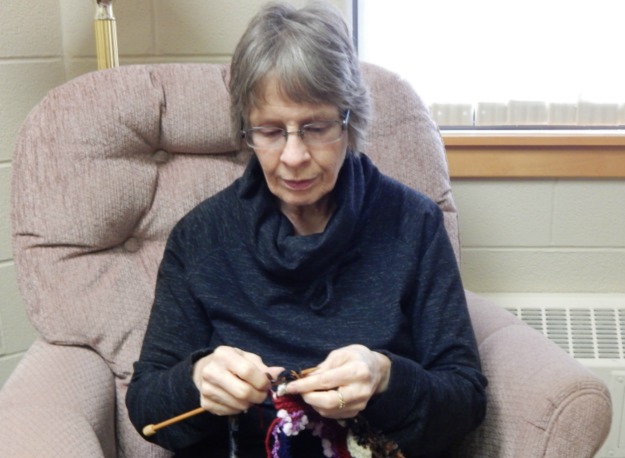 Volunteer, Nancy, sits in a chair knitting