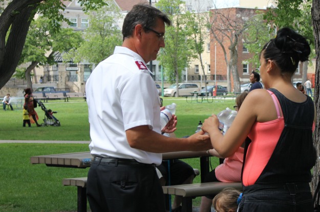 Major Rob Kerr (left) hands bottle water to woman in park