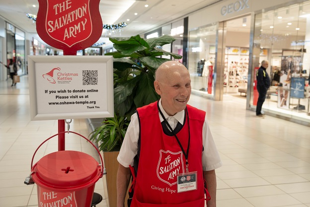 Kettle volunteer, Ted, stands behind red kettle at local mall