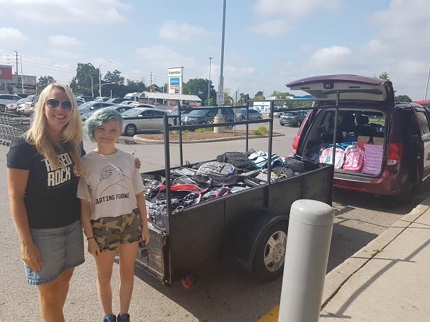 Trista stands alongside pick-up truck and van with donated backpacks