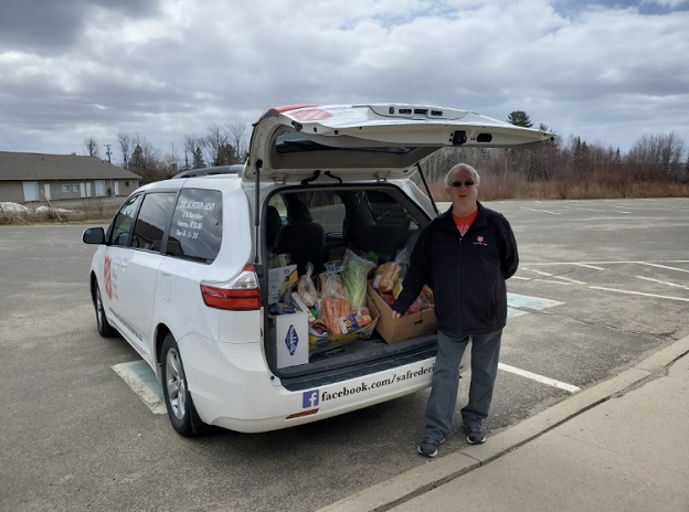Salvation Army volunteer stands in front of van full of food