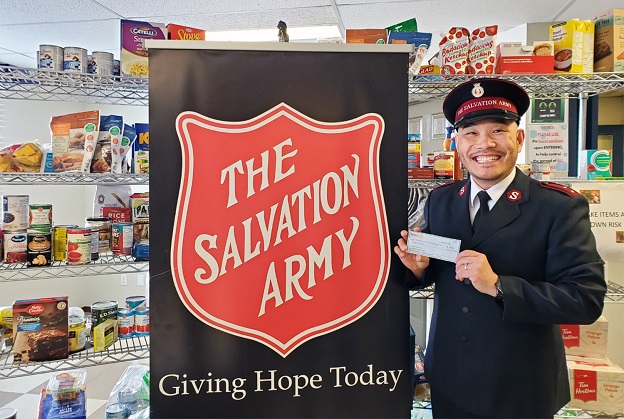 Captain Peter Kim stands beside Salvation Army banner holding grant from Alberta Government