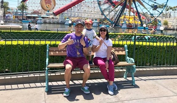 Adrian and his family sit on bench at theme park