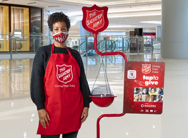 Kettle worker stands with mask and volunteer apron by iconic red kettle and tiptap machine
