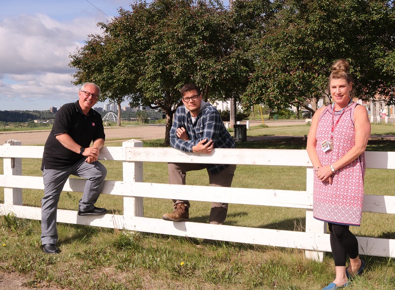 Standing by a white picket fence in an open field are Chaplain Doug, Ryan and Sarah