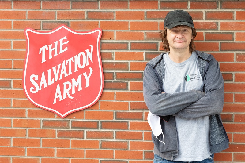 Norm stands in front of Harbour Light Toronto beside Salvation Army shield