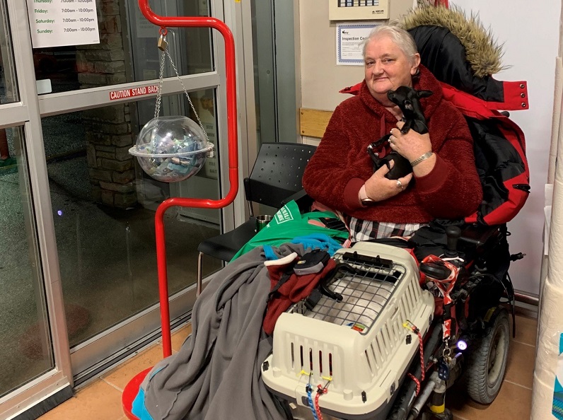 Linda B sits in wheelchair holding puppy by Salvation Army kettle