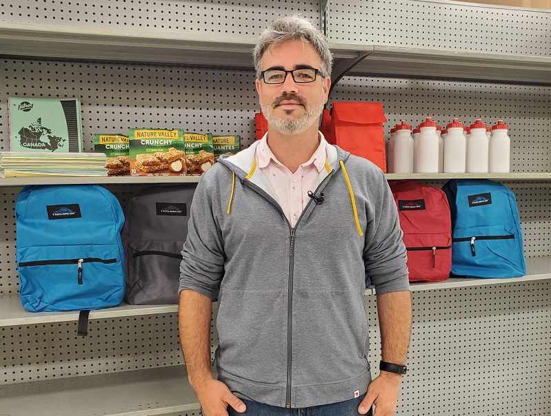 teacher stands in front of backpacks , water bottles and snacks