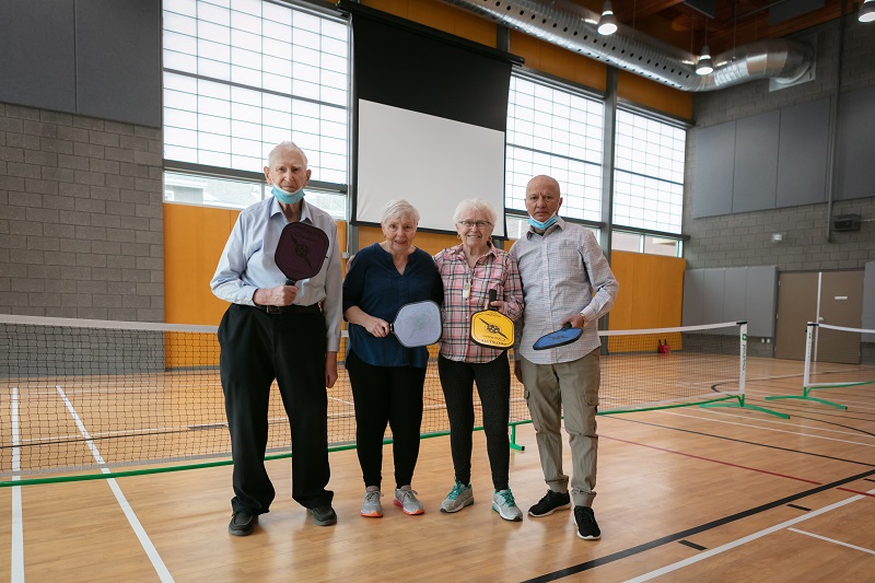 four seniors stand in pickleball court with paddles
