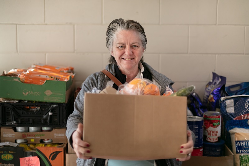 Sharon smiles holding a box of food from the food bank