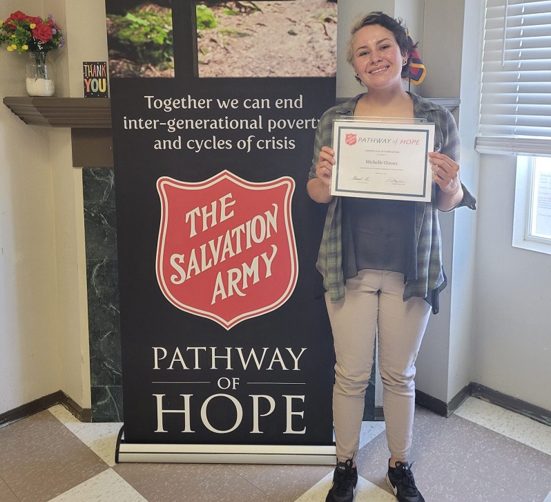 Michelle stands in front of Pathway of Hope sign holding her graduation certificate
