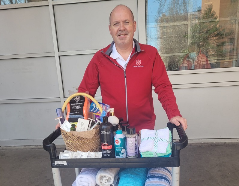 Major Danny Pinksen stands in front of cart with towels and soaps