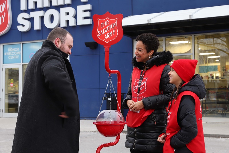 Donor puts money into red kettle while workers look on