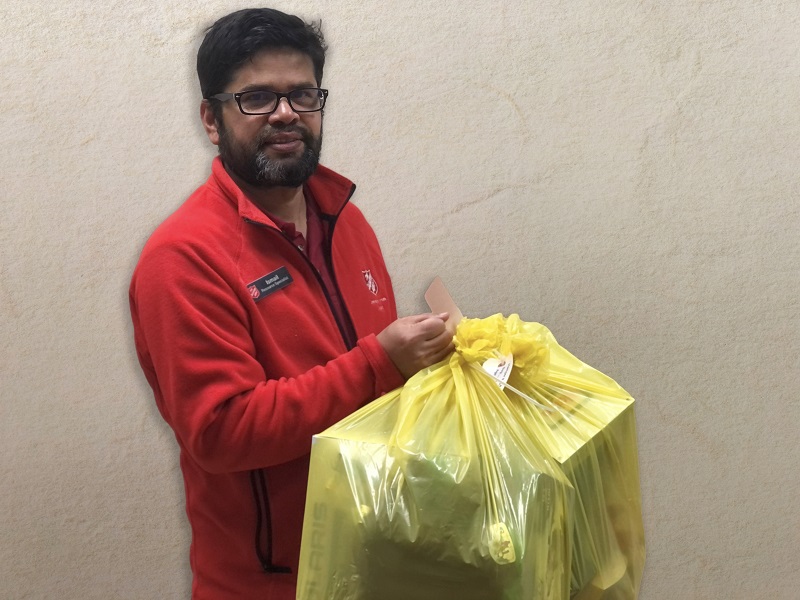 Salvation Army worker in red branded wear carries bag of toys for client
