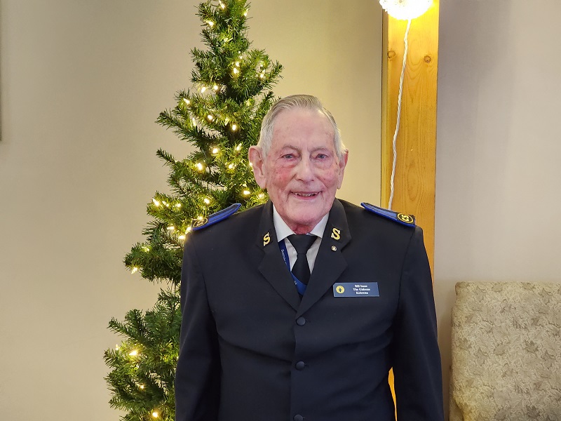 Bill wears his Salvation Army uniform and stands in front of Christmas Tree
