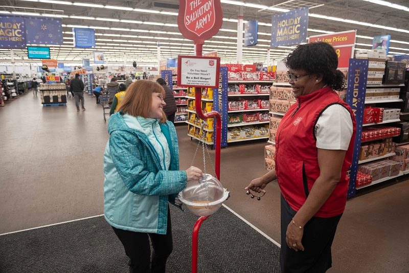 Salvation Army worker stands by kettle in Walmart while young woman makes donation