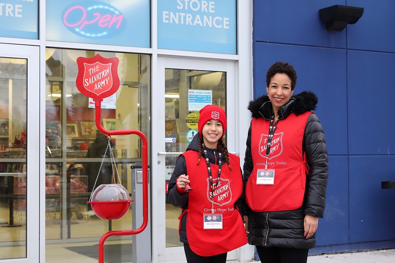 Two volunteers stand beside Salvation Army kettle