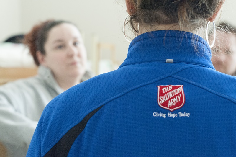 Salvation Army worker in blue jacket with Giving Hope Today on the back talks to client