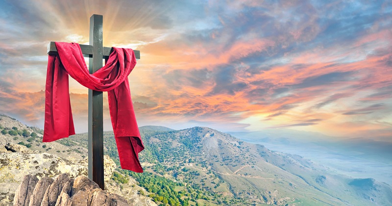 Cross on a hill is draped in crimson. Background is sunrise.