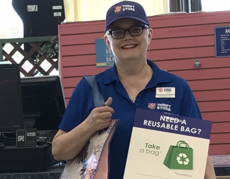 Thrift store worker holds reusable bag and sign offering them
