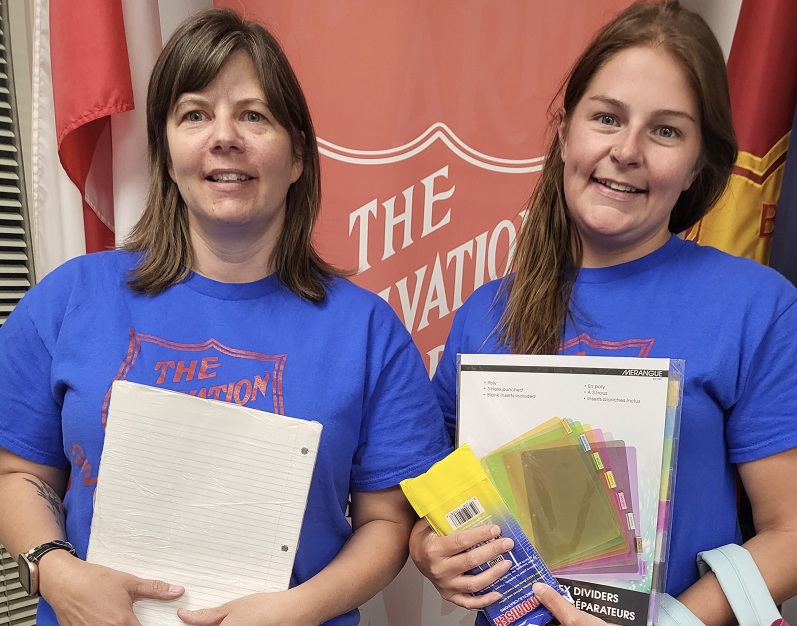Two Salvation Army staff hold school supplies-notepads and pens