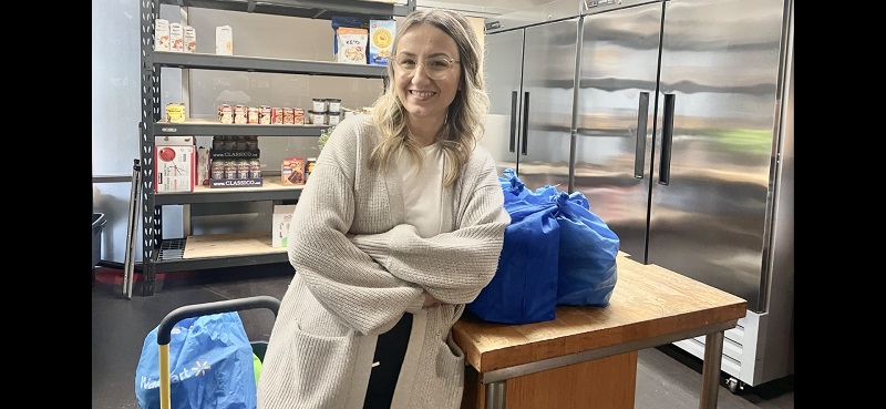 Salvation Army worker stands in food room beside packed bags of food for distribution