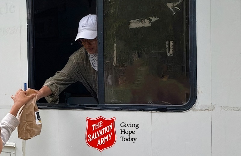 Volunteer hands breakfast bag from a Salvation Army mobile unit to student