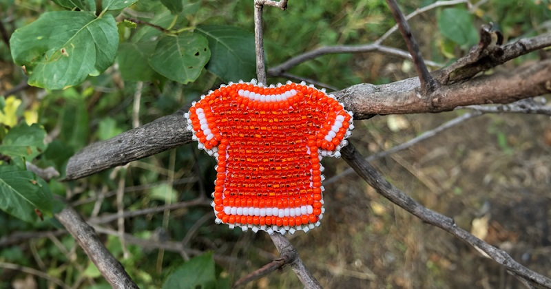 small beaded orange shirt hangs from tree branch