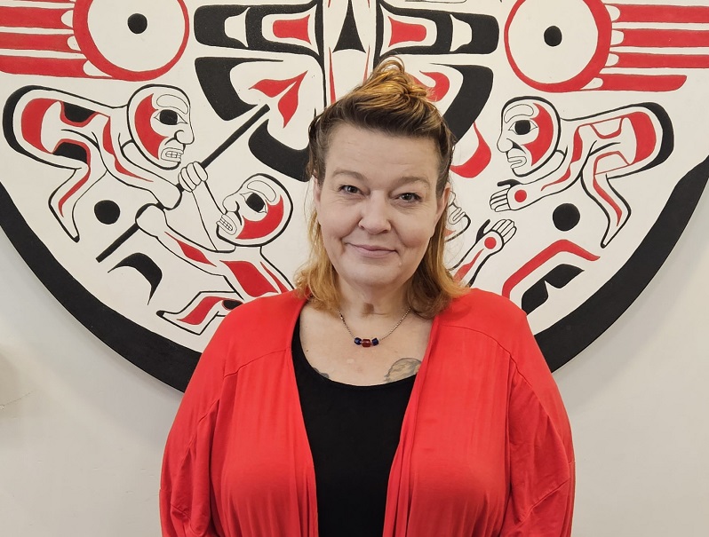 Breeze stands with red sweater and black top under Indigenous art