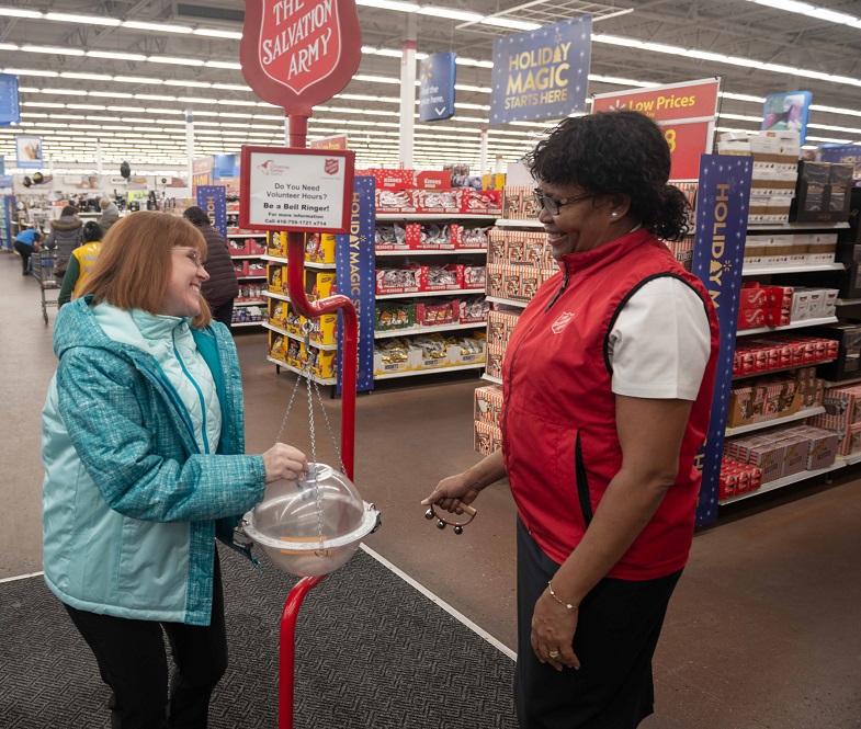 Woman puts donation in Christmas kettle. Salvation Army worker in branded vest looks on